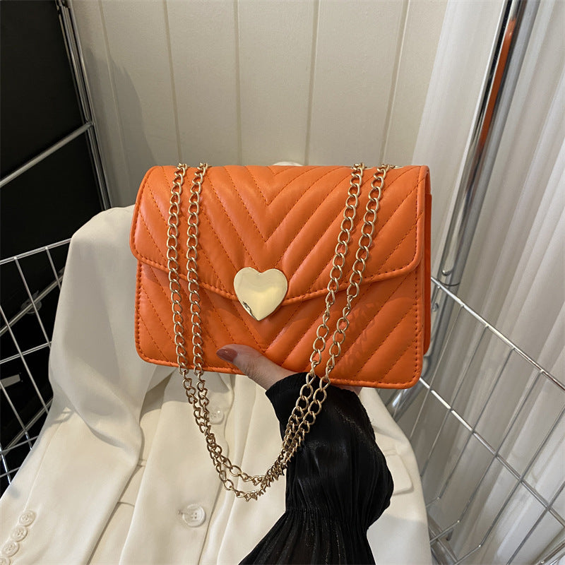 Chevron heart-lock chain crossbody bag in orange - model holding bag with gold double chain strap