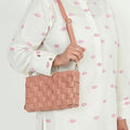 Woven leather crossbody clutch in blush pink - model wearing as crossbody with pink fish-print outfit