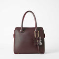 Maroon structured top handle handbag - model lifestyle shot wearing cream abaya in outdoor setting