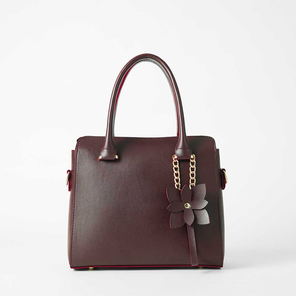 Maroon structured top handle handbag - model lifestyle shot wearing cream abaya in outdoor setting