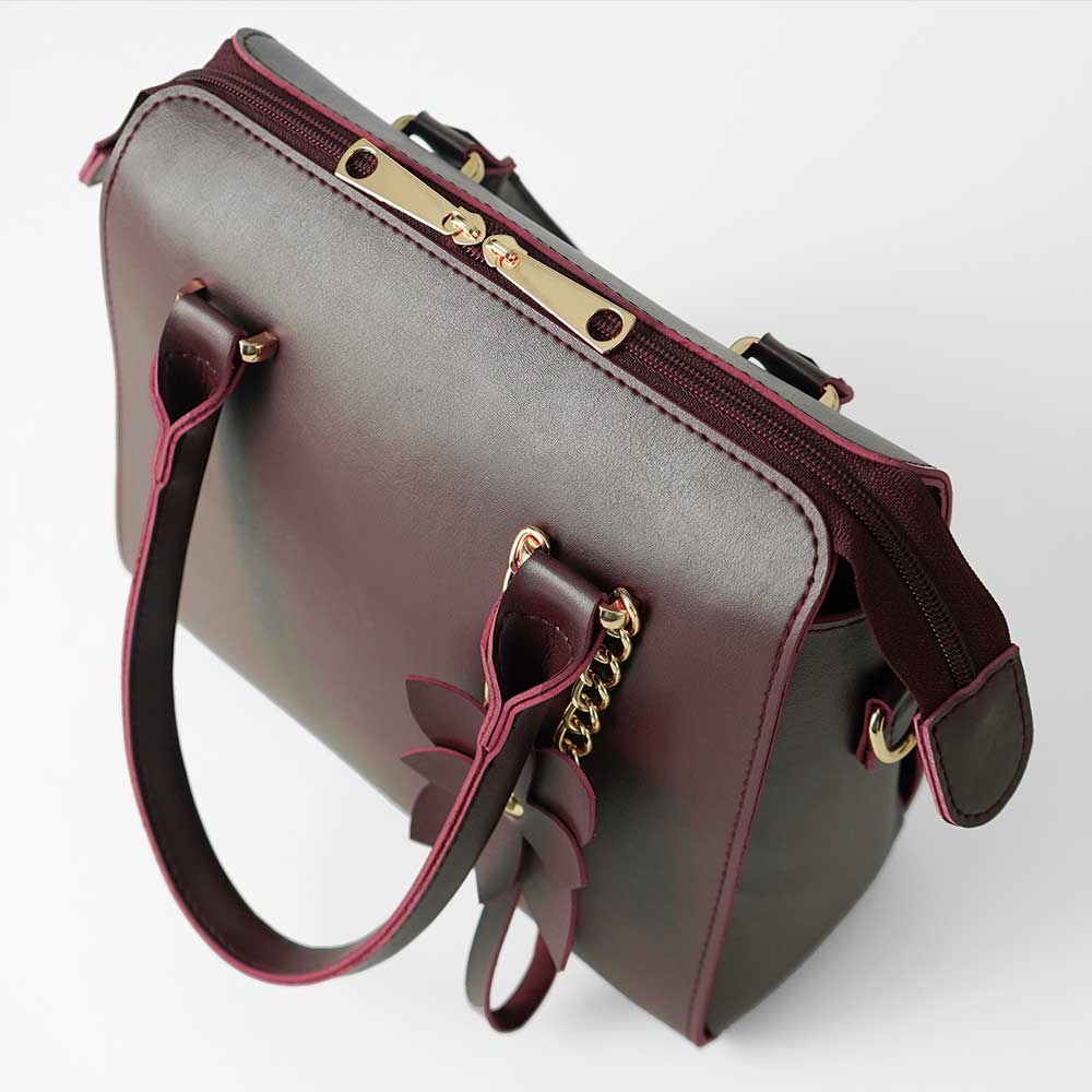 Maroon structured top handle handbag - model close-up holding bag showing gold chain charm and flower tab