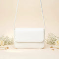 Magnetic crossbody bag in white - lifestyle front view with white flowers and gold chain accessories
