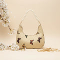 Rangon Ki Titli butterfly print pearl handle bag - lifestyle flat lay with white cherry blossoms and gold chain strap